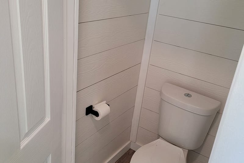 Toilet area with white shiplap walls and a wood-look floor