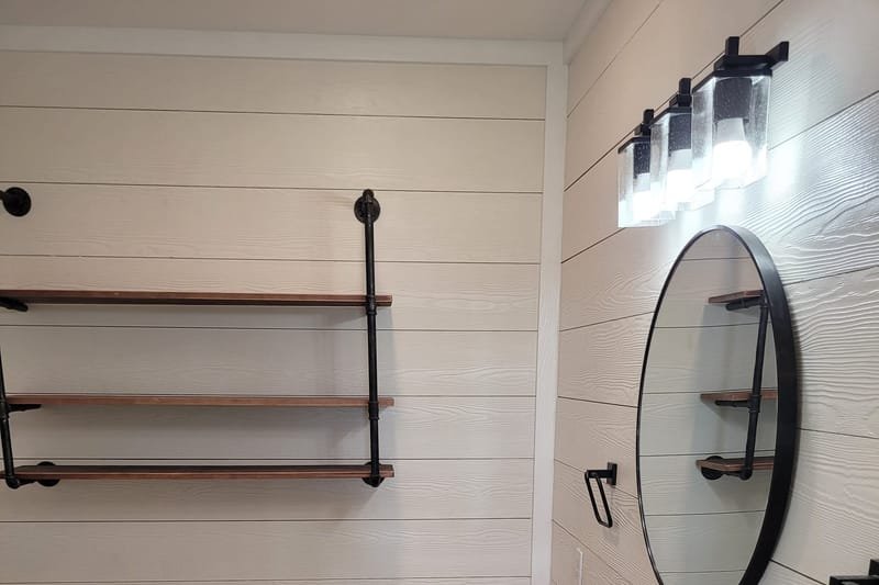 Bathroom with shiplap walls, a black vanity top, round mirror and pipe shelves