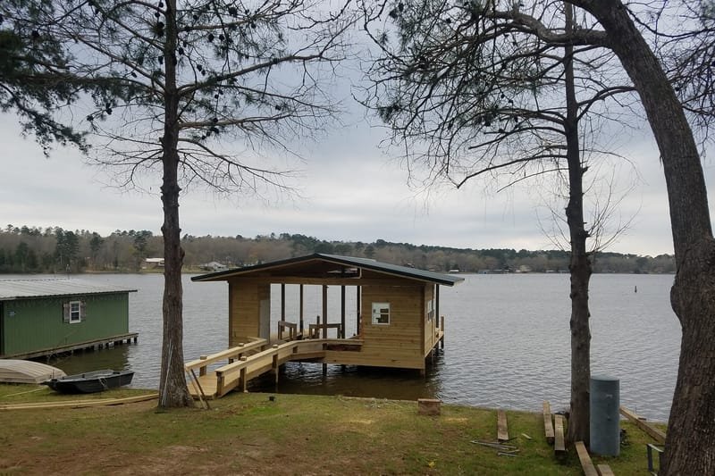 New boathouse on the lake, seen from the shore between two pines