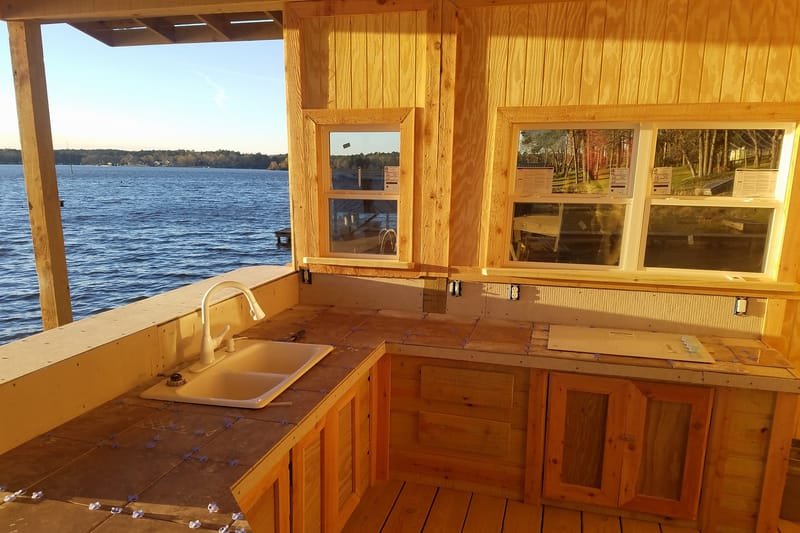 Wood cabinets, a tile counter and a sink under boathouse windows