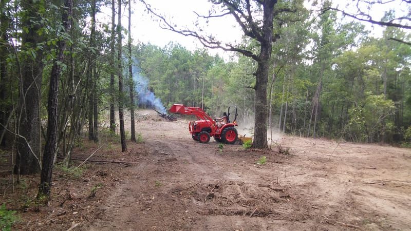 Tractor working near a burning brush pile on a cleared lot