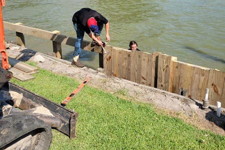 Crew setting bulkhead boards along a canal, with an excavator nearby