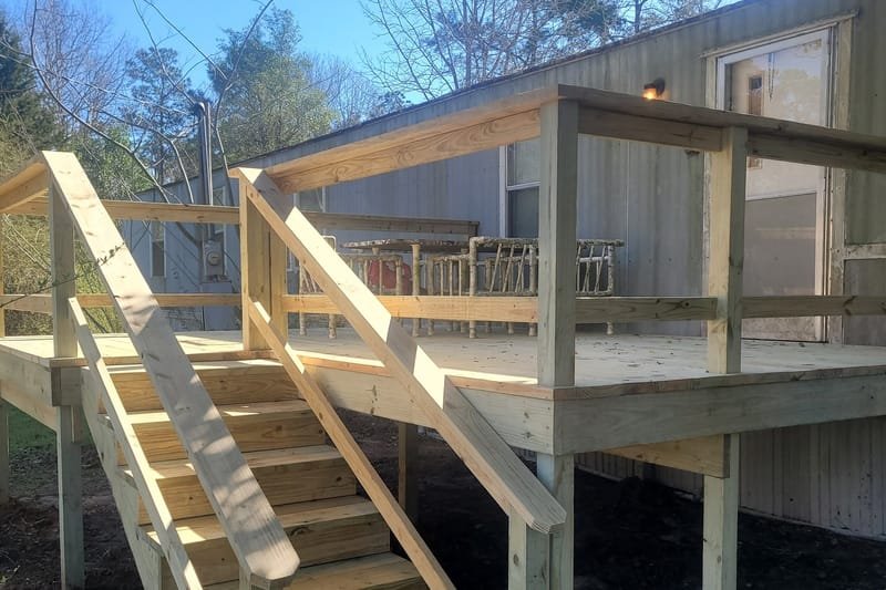 New pressure-treated deck with railings and stairs beside a mobile home