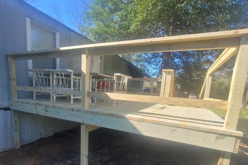 Raised pressure-treated deck with a railing on the side of a home