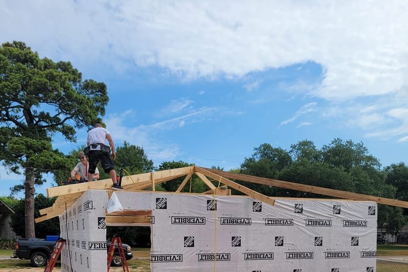 Detached garage framed and wrapped, with a crew member on the roof trusses
