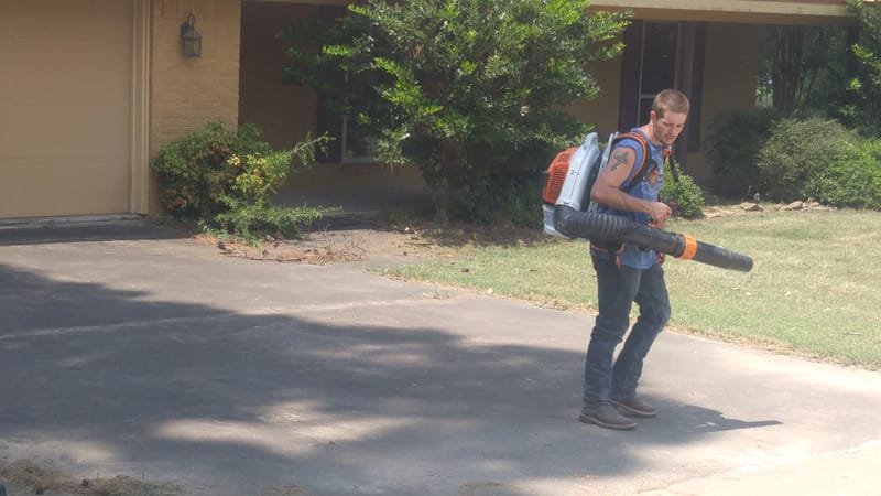 Crew member blowing clippings off a concrete driveway