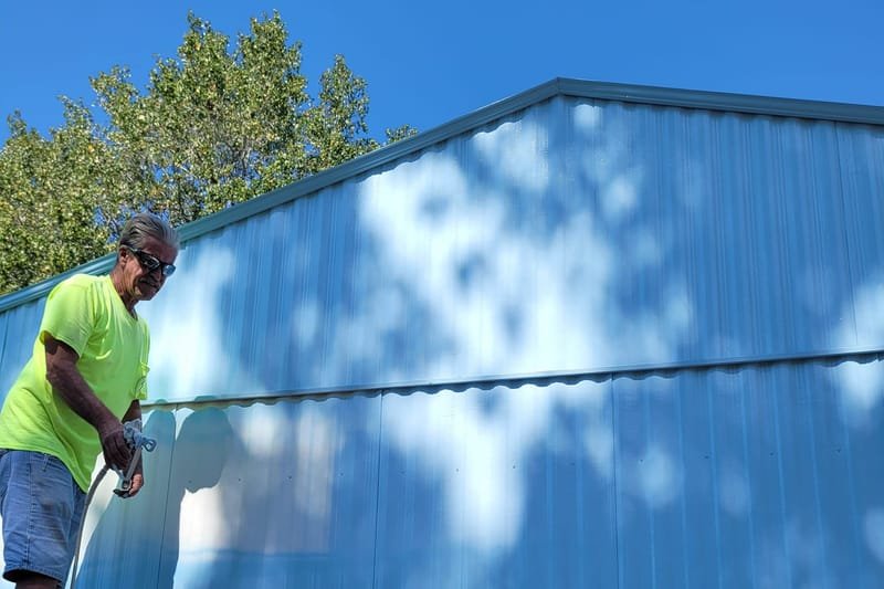 Crew member spraying light blue paint on a mobile home
