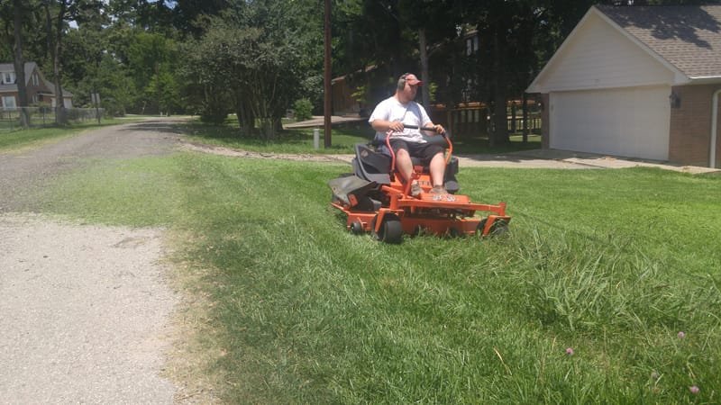 Mowing tall grass beside a gravel driveway