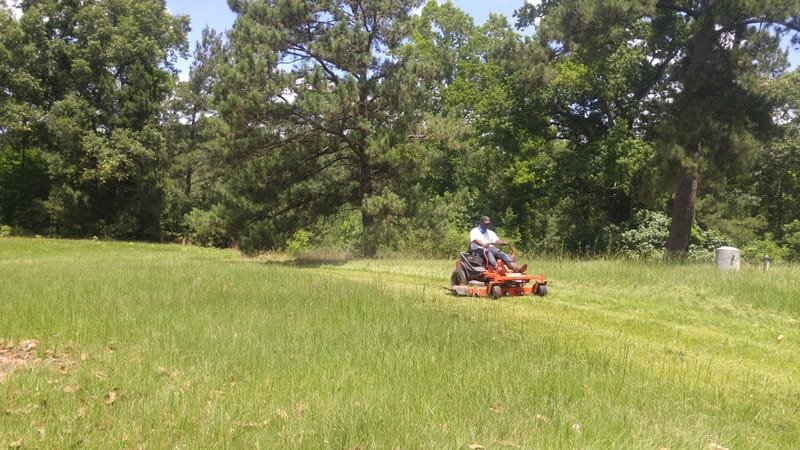 Zero-turn mower cutting tall grass on an open lot