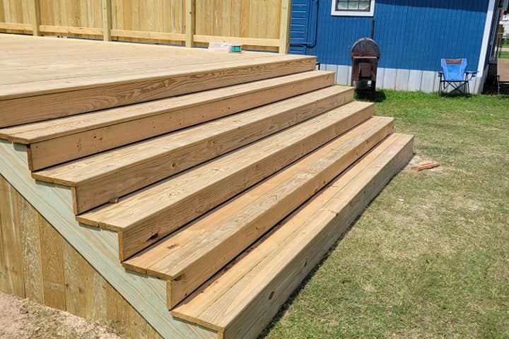 Pressure-treated deck with wide steps and a privacy wall beside a blue house