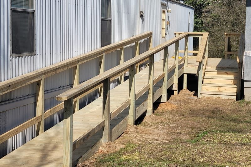 Wooden ramp with handrails leading to a landing at a mobile home door