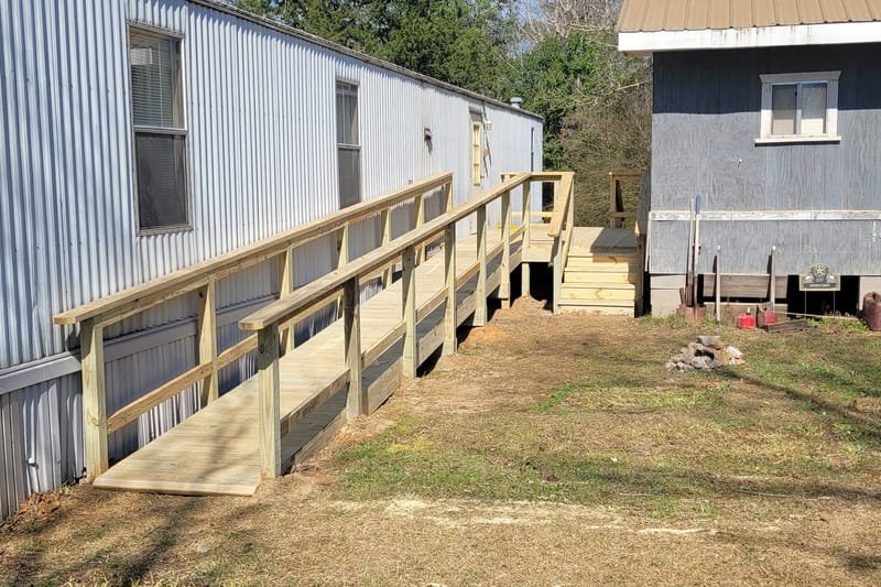 Long wooden wheelchair ramp with handrails along a mobile home