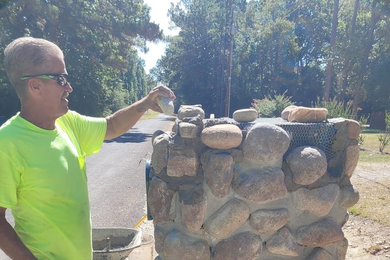 Crew member setting river rock on a mailbox column
