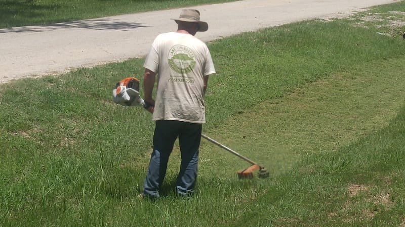 Crew member string-trimming grass along a driveway