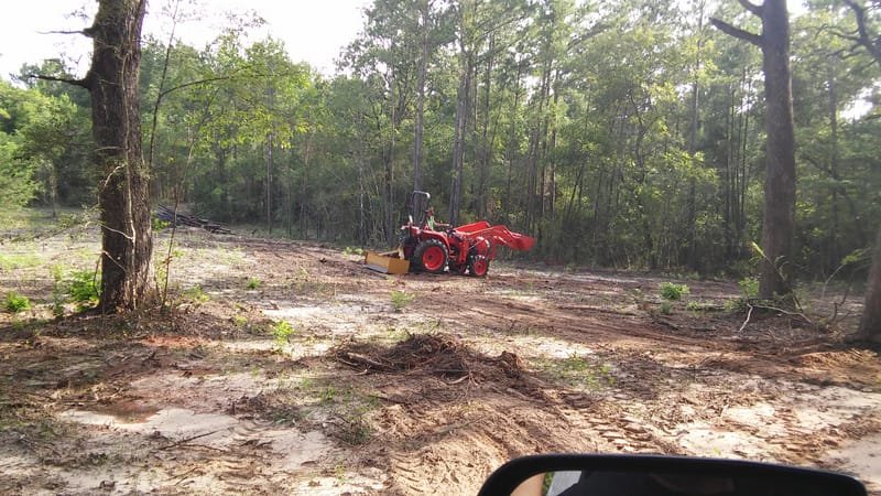Tractor on a freshly cleared lot with the larger trees left standing