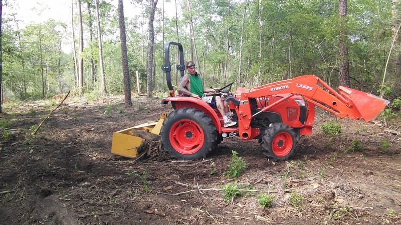 Tractor with a front loader and rear cutter clearing brush between pines