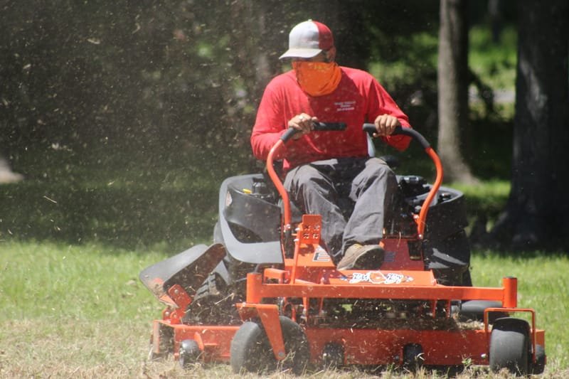 Crew member on a zero-turn mower cutting dry grass